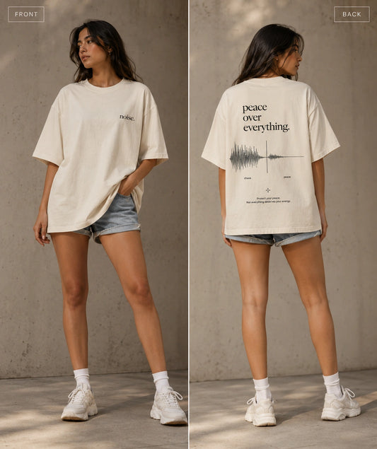 A model is shown from the front and back wearing an oversized cream-colored graphic t-shirt paired with denim shorts, white socks, and sneakers, set against a textured concrete wall background.
