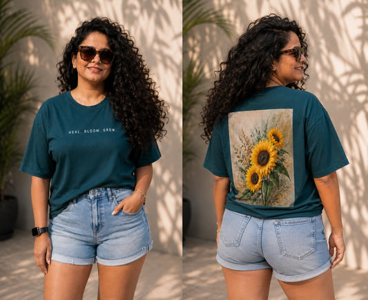 Woman wearing a teal t-shirt with text on the front and sunflower design on the back, standing outdoors.