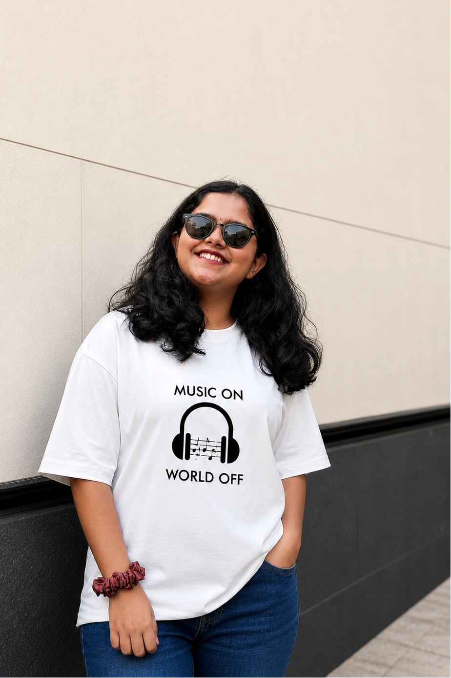 Person wearing a white t-shirt with a music-themed design, standing against a plain wall.