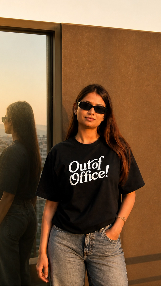 Person wearing a black t-shirt with 'Out of Office!' text, standing against a reflective surface.