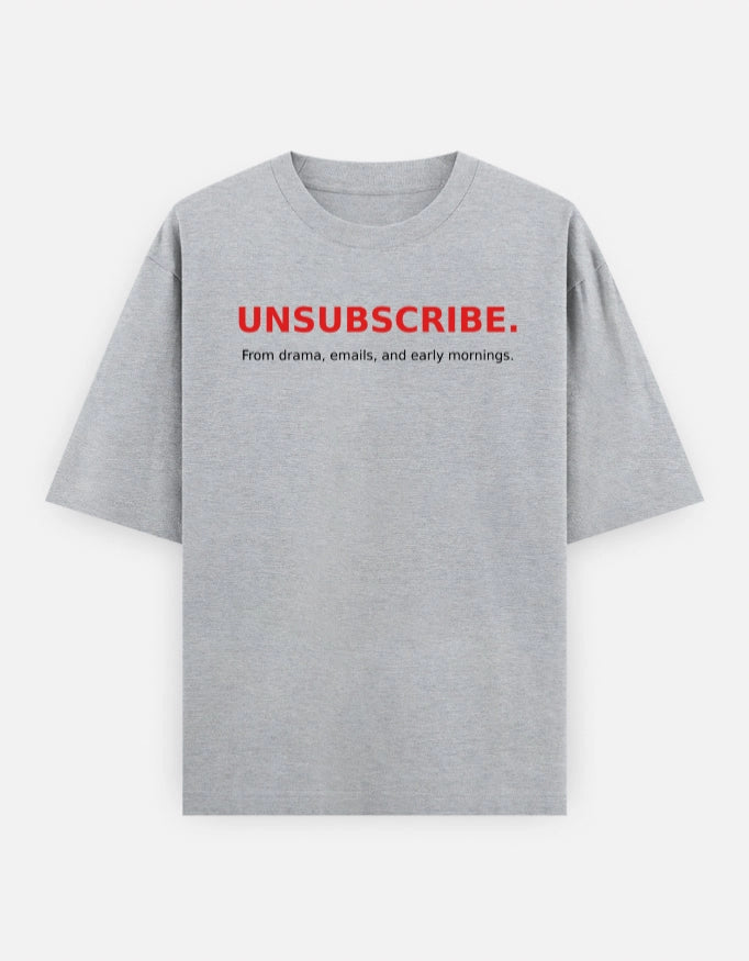 Front view of The Unserious Studio oversized unisex T-shirt with "Unsubscribe from Office Drama" slogan in black on white cotton fabric.